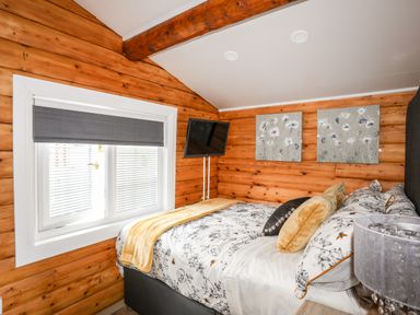 A bedroom with a bed near a window with blinds and paintings on wooden walls at Ty Coed - 63 Bronaber near Trawsfynydd
