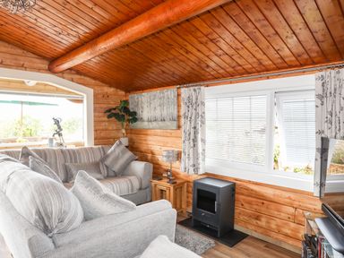 A living room with grey sofas a small stove and large windows at Ty Coed - 63 in Bronaber near Trawsfynydd