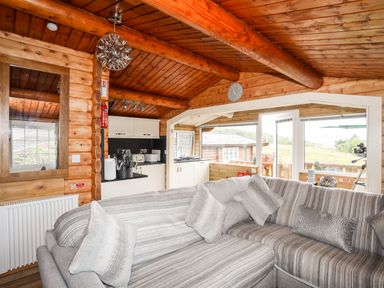 A living area with a striped gray sofa and kitchen cabinets in a wooden cabin at Ty Coed - 63 Bronaber near Trawsfynydd