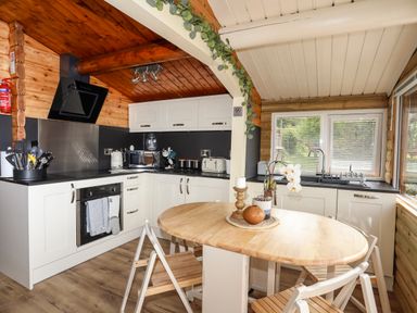 A kitchen with white cabinets wooden table chairs and appliances at Ty Coed - 63 Bronaber near Trawsfynydd