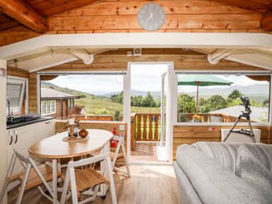 A kitchen and dining area with wooden table and chairs a sofa and a door leading to an outdoor deck with a view at Ty Coed - 63 in Bronaber near Trawsfynydd