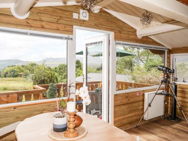 A wooden interior room with a round table holding a plant and candle a telescope by the window and a door leading to an outdoor deck at Ty Coed - 63 in Bronaber near Trawsfynydd
