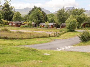 A rural area with wooden cabins trees a road and mountains in the background at Ty Coed - 63 in Bronaber near Trawsfynydd