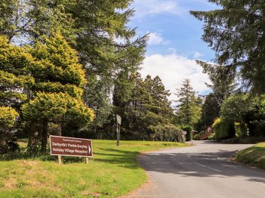 A road leading to holiday village reception surrounded by trees and a sign on grass at Ty Coed - 63 in Bronaber near Trawsfynydd