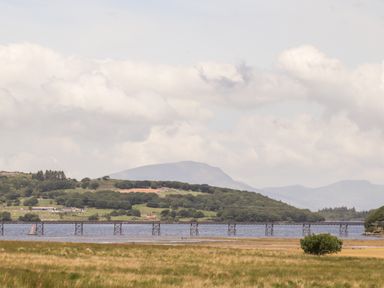 A landscape with grassy field in the foreground a body of water a bridge and hills with trees in the background at Ty Coed - 63 in Bronaber near Trawsfynydd