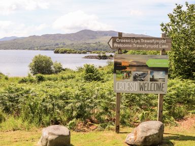 A lakeside view with a welcome sign for Trawsfynydd Lake and surrounding greenery at Ty Coed - 63 in Bronaber near Trawsfynydd