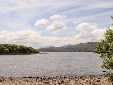 A lake with a rocky shore surrounded by trees and hills under a cloudy sky at Ty Coed - 63 in Bronaber near Trawsfynydd