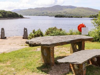 A stone table and bench on grass near a lake with mountains in the background at Ty Coed - 63 in Bronaber near Trawsfynydd