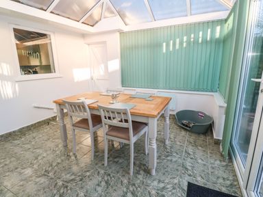 A conservatory with a wooden table and four chairs with placemats and a pet bed on a tiled floor at Dunes View in Cubert