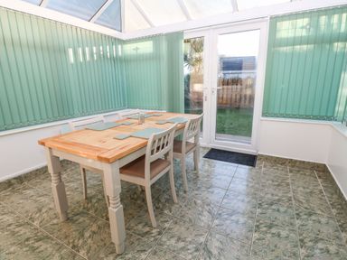A dining area with a wooden table and chairs surrounded by windows with green vertical blinds at Dunes View in Cubert
