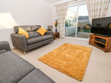 A living room with two grey sofas yellow cushions a yellow rug a wooden TV stand with a TV and sliding glass doors at Dunes View in Cubert