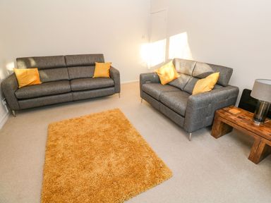 A living room with two gray sofas with yellow cushions a wooden side table with a lamp and an orange rug at Dunes View in Cubert