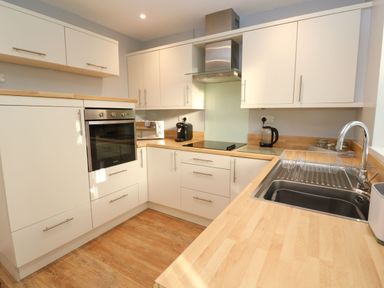 A kitchen with wooden countertops white cabinets built in oven microwave coffee machine electric stove and stainless steel sink at Dunes View in Cubert