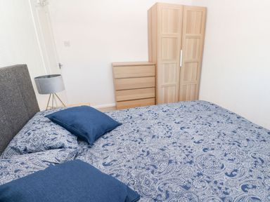 A bedroom with a bed with blue patterned bedding blue pillows a wooden wardrobe and chest of drawers at Dunes View in Cubert