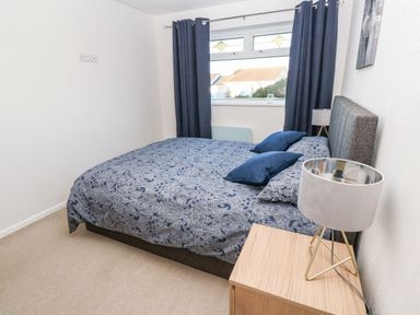 A bedroom with a bed covered in blue patterned bedding two blue pillows a wooden nightstand with a lamp and a window with dark curtains at Dunes View in Cubert