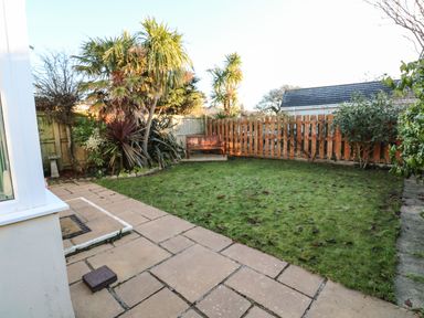 A small fenced garden with grass a wooden bench palm trees and paving stones at Dunes View in Cubert