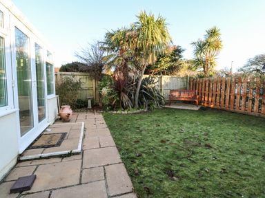 A garden with a paved patio area palm trees a wooden bench and a fenced lawn at Dunes View in Cubert