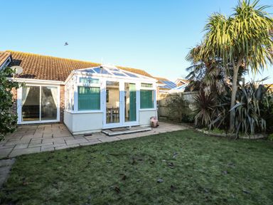 A backyard garden with a lawn patio and conservatory attached to a house at Dunes View in Cubert