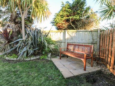 A wooden bench on a paved area next to a garden with plants and trees by a wooden fence at Dunes View in Cubert