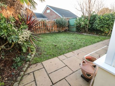 A garden with a grass lawn a wooden fence green shed and a tiled patio with a terracotta planter at Dunes View in Cubert