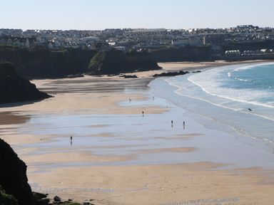 A beach with people walking near the shoreline and houses on cliffs in the background at Dunes View in Cubert
