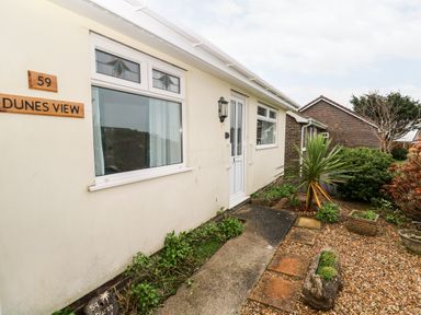 The exterior entrance of a house with cream walls a white door decorative windows and garden plants at Dunes View in Cubert