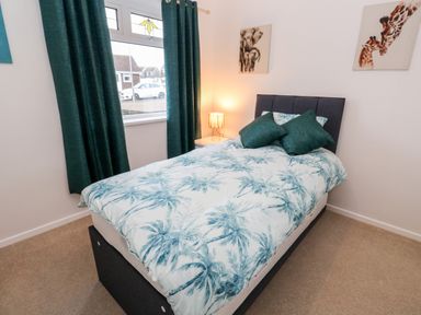 A bedroom with a single bed with palm tree bedding two green pillows a bedside table with a lamp green curtains and animal wall art at Dunes View in Cubert