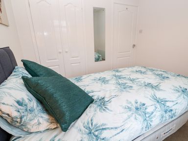 A bedroom with a bed covered in palm tree patterned bedding two green pillows a mirrored door and a white door at Dunes View in Cubert