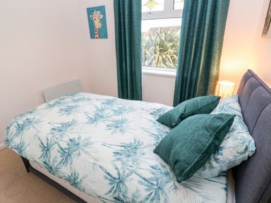 A bedroom with a bed that has palm tree patterned bedding teal pillows green curtains and a giraffe wall art at Dunes View in Cubert