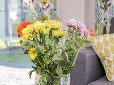 A vase with yellow pink and orange flowers on a table next to a grey sofa with patterned cushions at Jeans Place in East Heslerton near West Heslerton