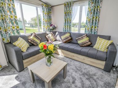 A living room with a gray sectional sofa, patterned cushions, floral curtains, and a wooden coffee table with flowers at Jeans Place in East Heslerton near West Heslerton