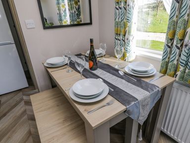 A dining table set with plates glasses cutlery and a bottle by a window with patterned curtains at Jeans Place in East Heslerton near West Heslerton