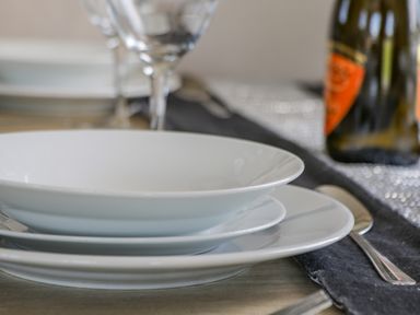 A dining table set with stacked white plates a spoon and glassware at Jeans Place in East Heslerton near West Heslerton