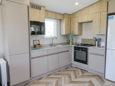 A kitchen with wooden and beige cabinets a microwave oven sink with a faucet a stove an oven a refrigerator and a vase with flowers at Jeans Place in East Heslerton near West Heslerton