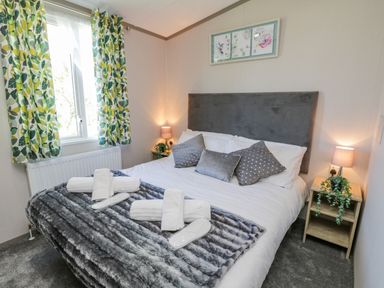 A bedroom with a double bed pillows and a gray blanket next to a window with leaf patterned curtains at Jeans Place East Heslerton near West Heslerton