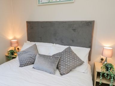 A bedroom with a bed with grey and white pillows two bedside tables with lamps and plants at Jeans Place in East Heslerton near West Heslerton