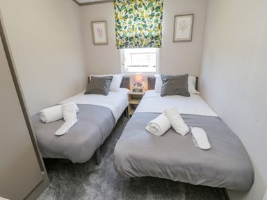 A bedroom with two single beds each with grey throws pillows and folded towels on a carpeted floor at Jeans Place in East Heslerton near West Heslerton