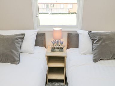 A bedroom with two single beds separated by a wooden nightstand with a lamp and floral decor at Jeans Place in East Heslerton near West Heslerton