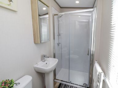 A bathroom with a toilet, pedestal sink, mirror cabinet, glass shower enclosure, towel rack, and window at Jean's Place in East Heslerton near West Heslerton