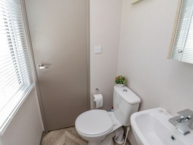 A small bathroom with a toilet and sink next to a beige door and window with blinds at Jeans Place in East Heslerton near West Heslerton