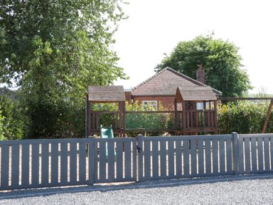 A fenced outdoor play area with a wooden climbing structure and slide in a garden at Jeans Place in East Heslerton near West Heslerton
