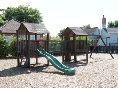 A wooden playground structure with two slides climbing net and a swing set in a wood chip covered yard at Jeans Place in East Heslerton near West Heslerton