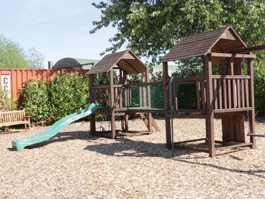 A playground with wooden climbing structures green slide and a wooden bench at Jeans Place in East Heslerton near West Heslerton
