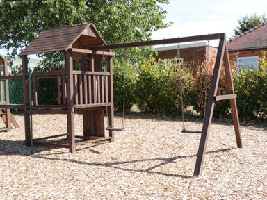A wooden playground structure with two swings and a small playhouse in a garden area at Jeans Place in East Heslerton near West Heslerton