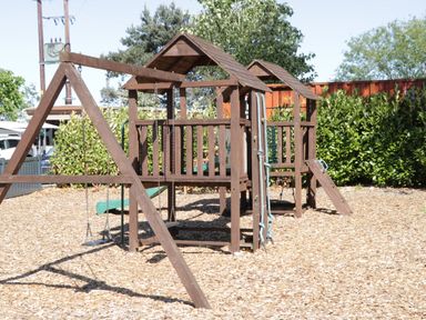 An outdoor wooden playground structure with swings slide climbing features and a wood chip ground surface at Jean's Place in East Heslerton near West Heslerton