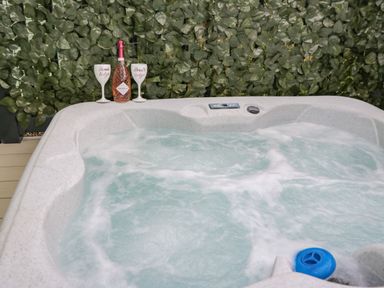 A bubbling hot tub with a bottle of prosecco and two glasses on the edge near a wall of green leaves at Jeans Place in East Heslerton near West Heslerton