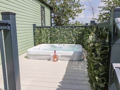 An outdoor hot tub on a deck with green leaf privacy screens and a bottle with two glasses at Jeans Place in East Heslerton near West Heslerton