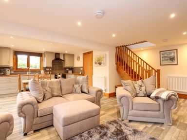 An open living room and kitchen area with beige sofas and wooden stairs at Little Lodge in Pentney near Kings Lynn