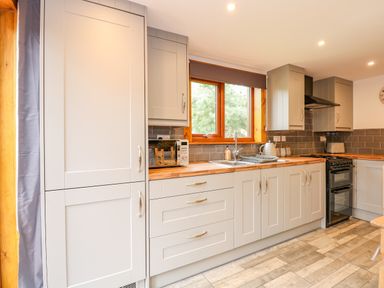 A kitchen with grey cabinets wooden countertops a window microwave sink and stove at Little Lodge Pentney near Kings Lynn