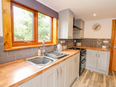 A kitchen with grey cabinets wooden countertops a sink and stove under a window at Little Lodge in Pentney near Kings Lynn
